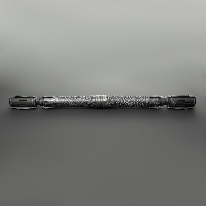 A long, cylindrical metallic tool or accessory with engraved swirling patterns, shown horizontally against a smooth gray gradient background.